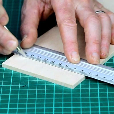 A balsa sheet, metal safety rule, craft knife and sanding block on a cutting mat