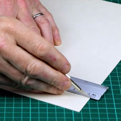 A cutting mat with a metal safety rule, a scalpel, a craft knife and a utility knife