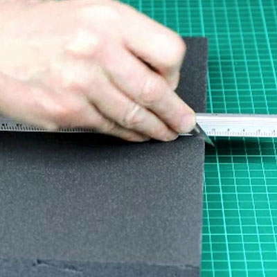 A block of grey Styrofoam on a green cutting mat beside a metal rule