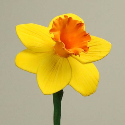 A row of finished clay daffodils with yellow petals and orange trumpets