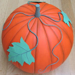 A finished orange foam pumpkin with a stalk and a green leaf, standing on grass